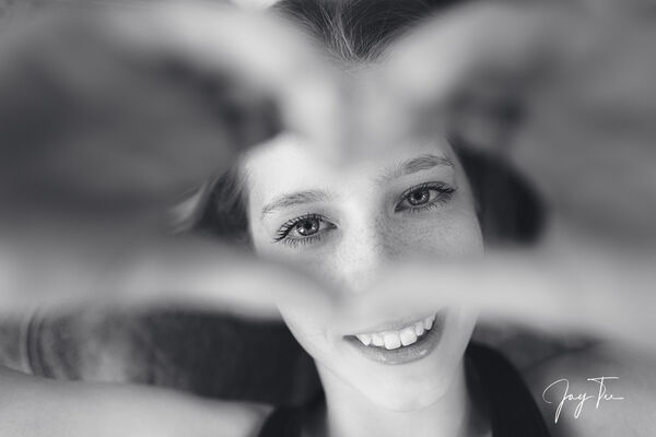 A teenager Girl smiles and looks through a hand heart.
