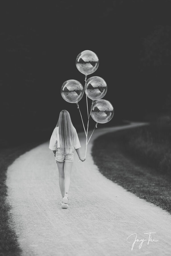 Monochrome portraiture of a young girl walking with four balloons.